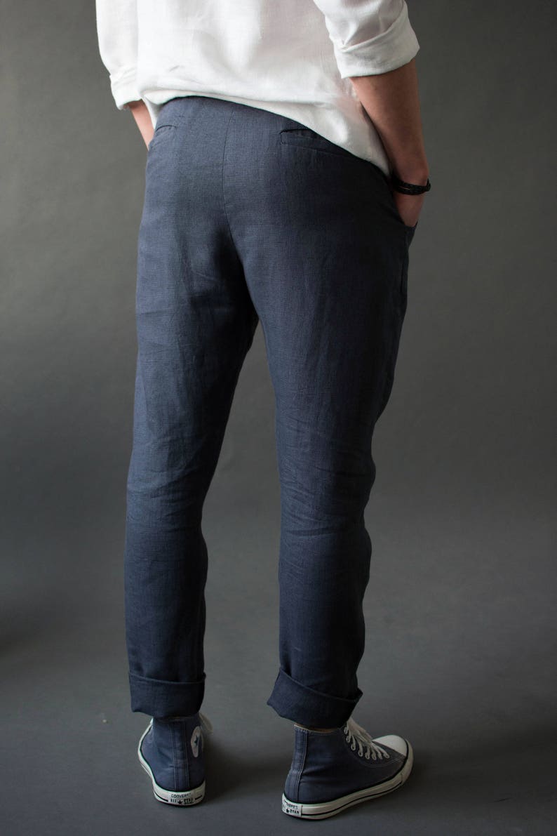 A man standing in the dark background, showing the back view of classic linen pants with two back pockets and a slightly tapered fit