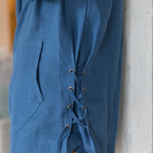 Op de afbeelding: Een blauw linnen shirt met een zijdelingse veterdetail. Het shirt heeft een zak aan de voorkant en is in de taille geknoopt.