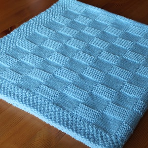 Może przedstawiać: Jasny błękitny, dziergany kocyk dla dziecka w kratkę.