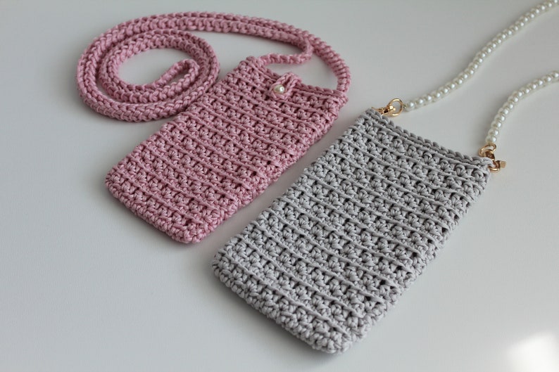 May include: Two crocheted phone pouches with straps. One pouch is pink with a crocheted strap and the other is gray with a pearl strap.
