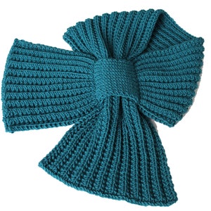 Może przedstawiać: Turkusowy, dzianinowy szalik z kokardą. Szalik wykonany jest z miękkiej przędzy i idealnie nadaje się do utrzymania ciepła w zimie.