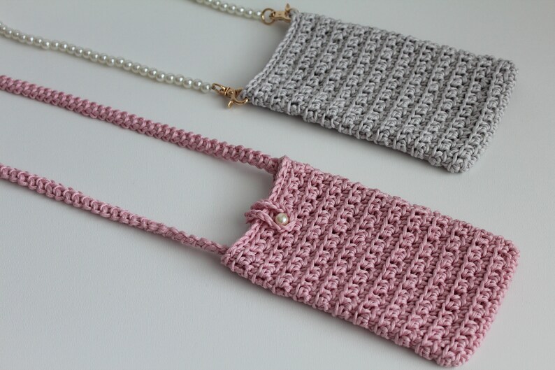 May include: Two crocheted phone pouches, one in pink and one in gray, with pearl and chain straps.