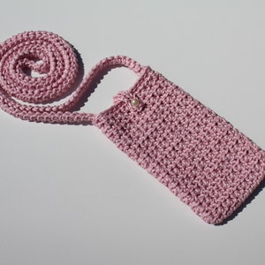 May include: A pink crocheted phone case with a long strap. The case has a pearl button closure.