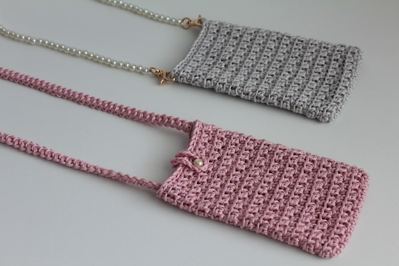 May include: Two crocheted phone pouches with pearl and chain straps. One pouch is gray and the other is pink.