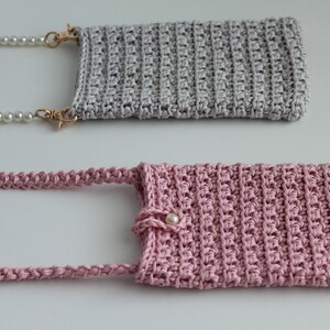May include: Two crocheted phone cases, one gray and one pink, with pearl chains attached. The pink case has a pearl button.