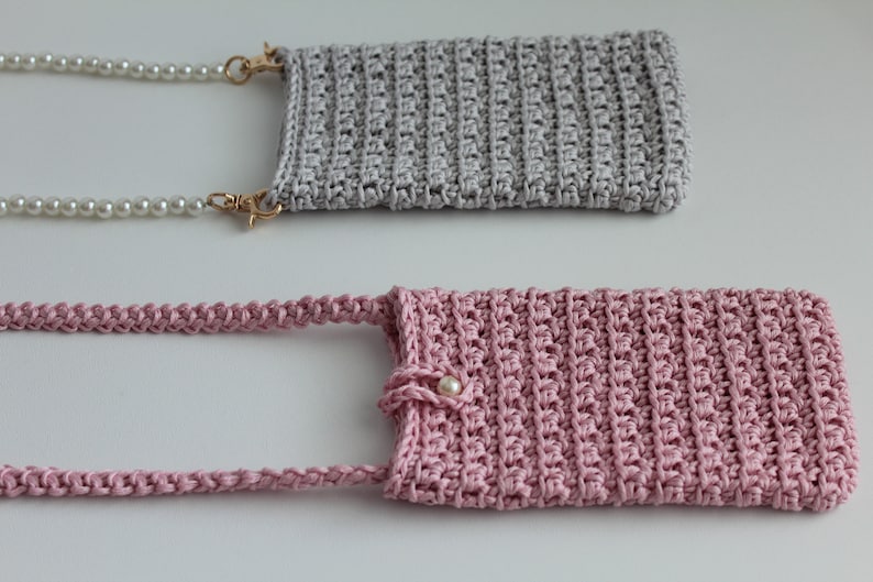 May include: Two crocheted phone cases, one gray and one pink, with pearl chains attached. The pink case has a pearl button.