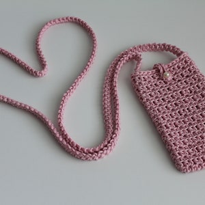 May include: A pink crocheted phone case with a pearl button and a long pink crocheted strap. The strap is shaped into a heart.