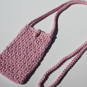 May include: A pink crocheted crossbody bag with a pearl accent. The bag is small and has a long strap.