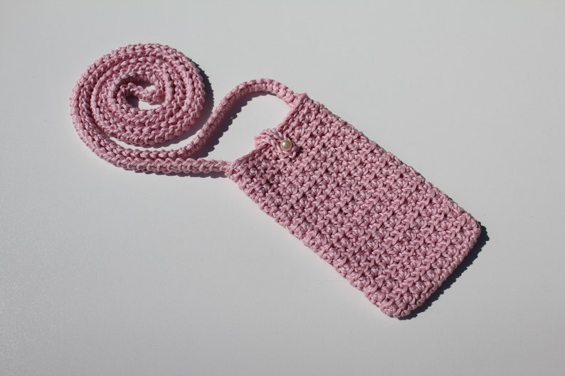 May include: A pink crocheted phone case with a pearl button closure and a long pink crocheted strap.