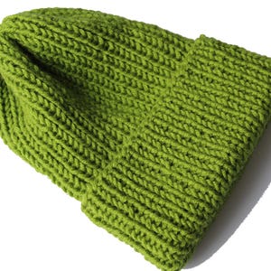 Könnte beinhalten: Eine limettengrüne Strickmütze mit umgeschlagenem Rand. Die Mütze ist aus dickem Garn gefertigt und hat eine gerippte Struktur. Die Mütze wird auf weißem Hintergrund gezeigt.