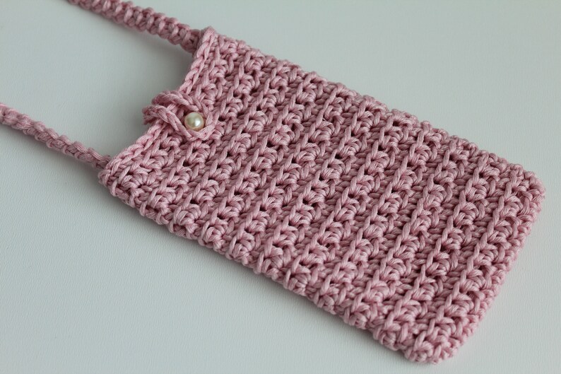 May include: A pink crocheted phone case with a pearl button and a long strap.