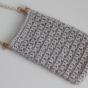 May include: A gray crocheted phone pouch with a pearl chain strap. The strap has gold clasps.