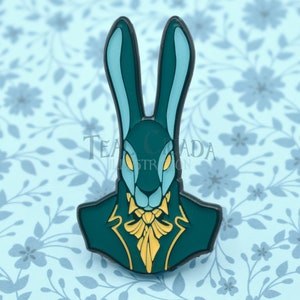May include: A teal blue enamel pin featuring a rabbit wearing a dark teal suit with a gold bow tie. The rabbit has black ears and yellow eyes.