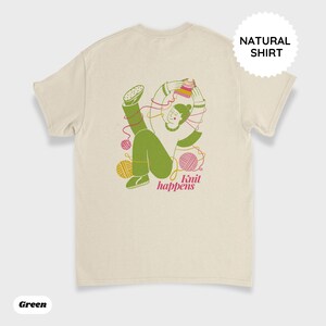 May include: A natural-colored t-shirt with a green illustration of a person knitting, surrounded by yarn balls and the text "Knit happens" in pink. The shirt also has a "NATURAL SHIRT" label.