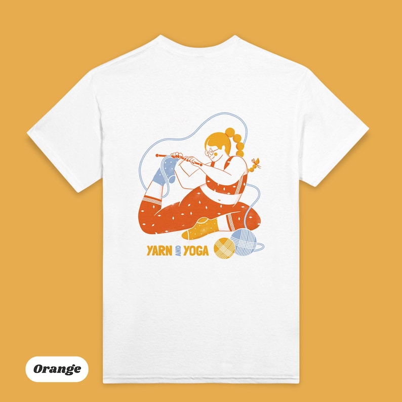 Op de afbeelding: Wit T-shirt met een afbeelding van een persoon die yoga doet en breit. De illustratie is in oranje, blauw en geel, met de woorden "Yarn and Yoga" eronder. Het T-shirt heeft een ronde hals.
