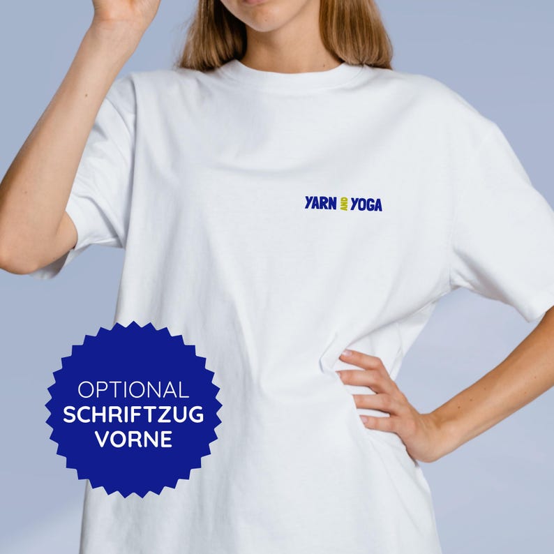 Op de afbeelding: Een wit t-shirt met de tekst "YARN YOGA" in blauw en groen. Het shirt heeft ook een blauwe stervormige afbeelding met de tekst "OPTIONAL SCHRIFTZUG VORNE".