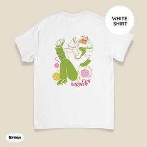 May include: White t-shirt with a green illustration of a person knitting, surrounded by yarn balls. The text "Knit happens" is in pink. A white circle with the words "WHITE SHIRT" is in the upper right corner.