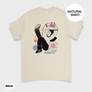 May include: Cream-colored t-shirt with a graphic of a person knitting, surrounded by yarn balls. The text "Knit happens" is below the illustration. A circular tag on the upper right reads "NATURAL SHIRT". The word "Black" is at the bottom left.