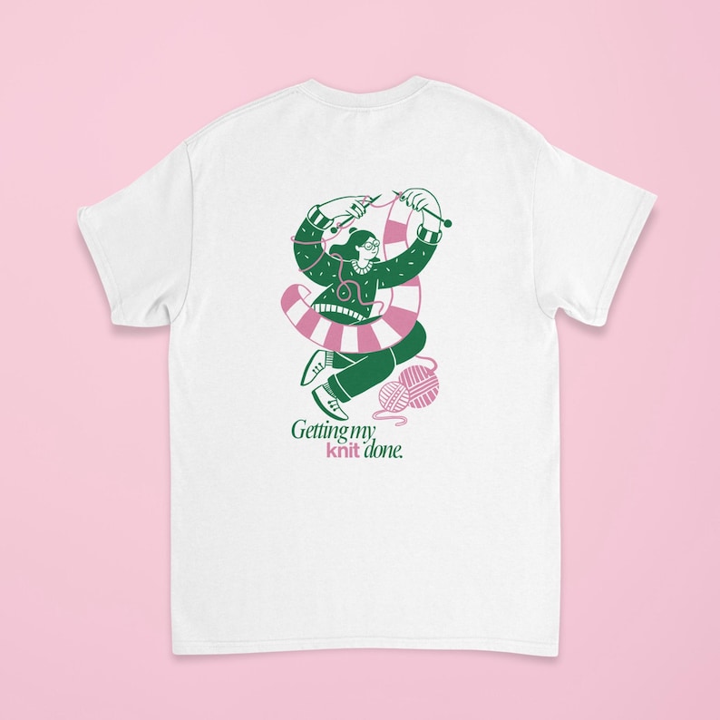 May include: White t-shirt with a graphic of a person knitting, wearing glasses and a green sweater. The person is surrounded by a pink and white striped design and green yarn. The text "Getting my knit done" is below the graphic.