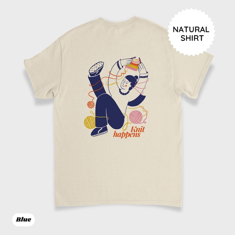 May include: Cream-colored t-shirt with a graphic of a person knitting, surrounded by yarn balls. The text "Knit happens" is below the illustration. The shirt also has the text "Natural Shirt" and "Blue" printed on it.