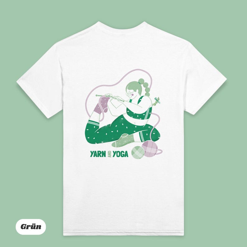 Op de afbeelding: Wit t-shirt met een groen en paarse illustratie van een persoon die in een yogahouding breit. De persoon draagt een groene legging met stippen en een bijpassende top. De tekst "YARN YOGA" staat eronder.