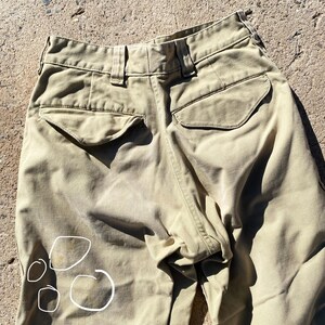 May include: Khaki-colored pants with two back pockets and a button closure. The pants show some staining on the front. The fabric appears to be a durable material, suitable for outdoor activities or workwear. The pants are shown from the back.