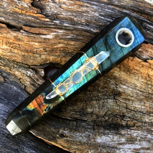 May include: A dark blue and green labradorite crystal pipe with a clear quartz crystal wrapped in gold wire. The pipe has a round hole for smoking.