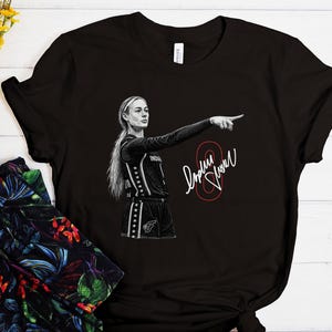 May include: A black short-sleeved t-shirt featuring a white graphic illustration of a basketball player pointing forward. The design includes a red outlined number eight and a white signature. The player wears a jersey with star accents.