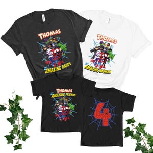 Puede incluir: Cuatro camisetas con gr&aacute;ficos de superh&eacute;roes. Una camiseta negra tiene el n&uacute;mero 4 rojo en una telara&ntilde;a. Las otras camisetas son negras y blancas con el nombre "Thomas" y personajes de superh&eacute;roes. Una dice "Amazing Daddy", otra dice "Amazing Mommy" y otra dice "Amazing Friends".
