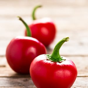 Op de afbeelding: Drie rode kerspaprika's met groene stelen op een houten oppervlak.