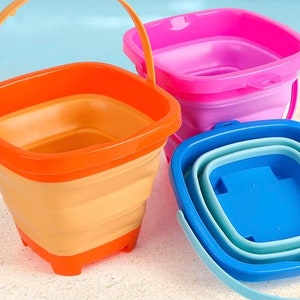 May include: Three foldable buckets in different colors: orange, pink, and blue. The buckets are made of plastic and have a square shape. They are ideal for beach trips or picnics.