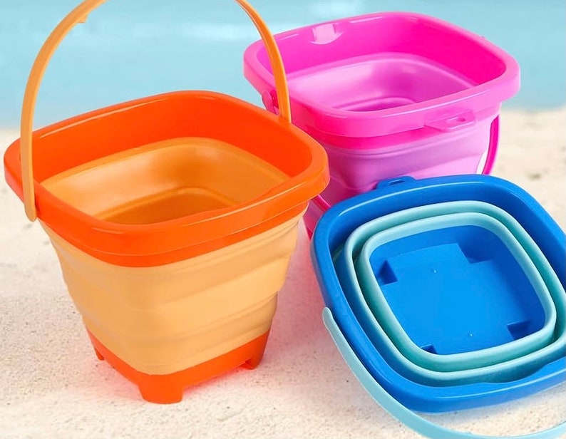 May include: Three foldable buckets in different colors: orange, pink, and blue. The buckets are made of plastic and have a square shape. They are ideal for beach trips or picnics.