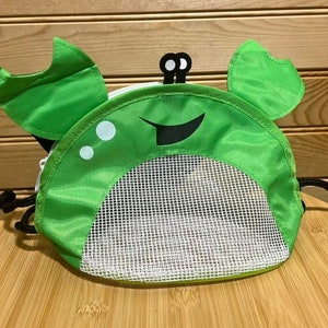 May include: Green mesh drawstring bag with a crab design. The bag has a white mesh bottom and a green fabric top with a black smiling face and white eyes.