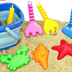May include: A blue folding bucket with a handle, a yellow, blue, and pink sand toys, and a set of colorful plastic sea creatures including a crab, starfish, seashell, and a seahorse.