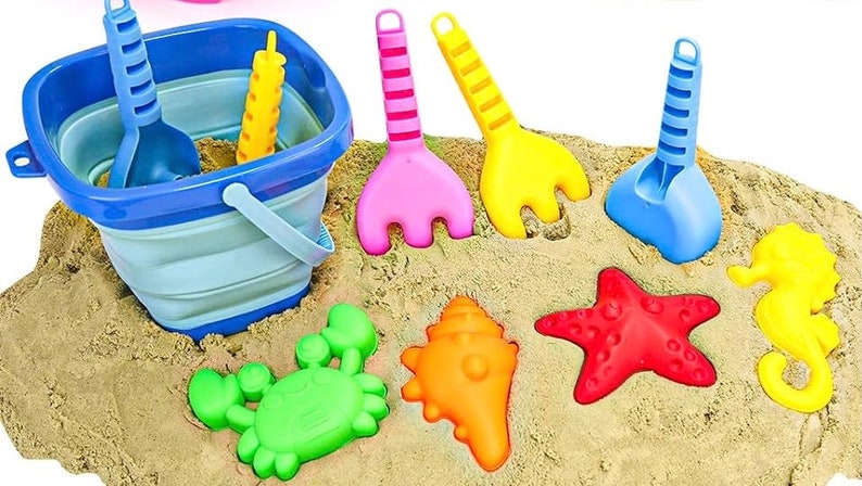 May include: A blue folding bucket with a handle, a yellow, blue, and pink sand toys, and a set of colorful plastic sea creatures including a crab, starfish, seashell, and a seahorse.