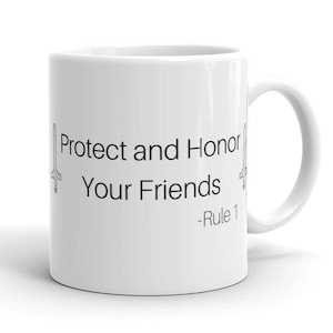 Pu&ograve; includere: Tazza in ceramica bianca con la scritta "Protect and Honor Your Friends - Rule 1" in nero. Il design include illustrazioni di spade su entrambi i lati del testo. La tazza ha un manico curvo.