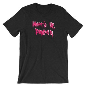 Puede incluir: Camiseta gris oscuro con la frase "What's Up, Danger" en rosa con letras goteando. La camiseta tiene mangas cortas y cuello redondo. El texto est&aacute; centrado en el pecho.