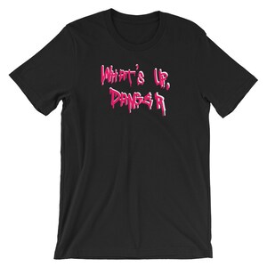 Puede incluir: Camiseta negra con la frase "What's Up, Danger" en rosa, con letras estilo goteo. La camiseta tiene mangas cortas y cuello redondo. El texto est&aacute; centrado en la parte delantera.