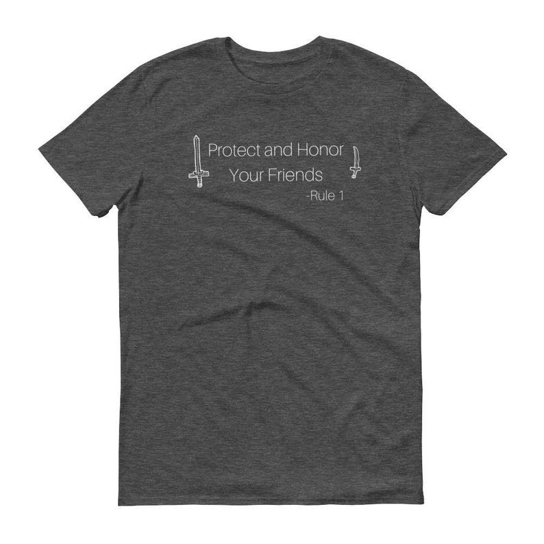 May include: Dark gray t-shirt with the text "Protect and Honor Your Friends - Rule 1" in white. The design includes two stylized sword illustrations, one on each side of the text. The shirt is made of a soft material.