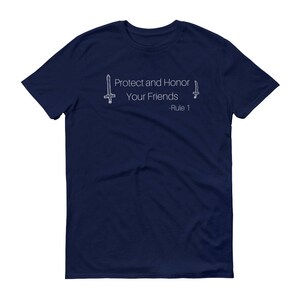 May include: Navy blue t-shirt with the text "Protect and Honor Your Friends - Rule 1" in white. The design includes line drawings of a sword and a dagger. The shirt is a short-sleeved crew neck.