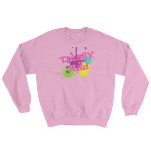 May include: A light pink sweatshirt with long sleeves. The front features the text "TOTALLY RAD" in a colorful, splattered design with pink, purple, green, blue, and yellow accents. The sweatshirt is a casual, comfortable style.
