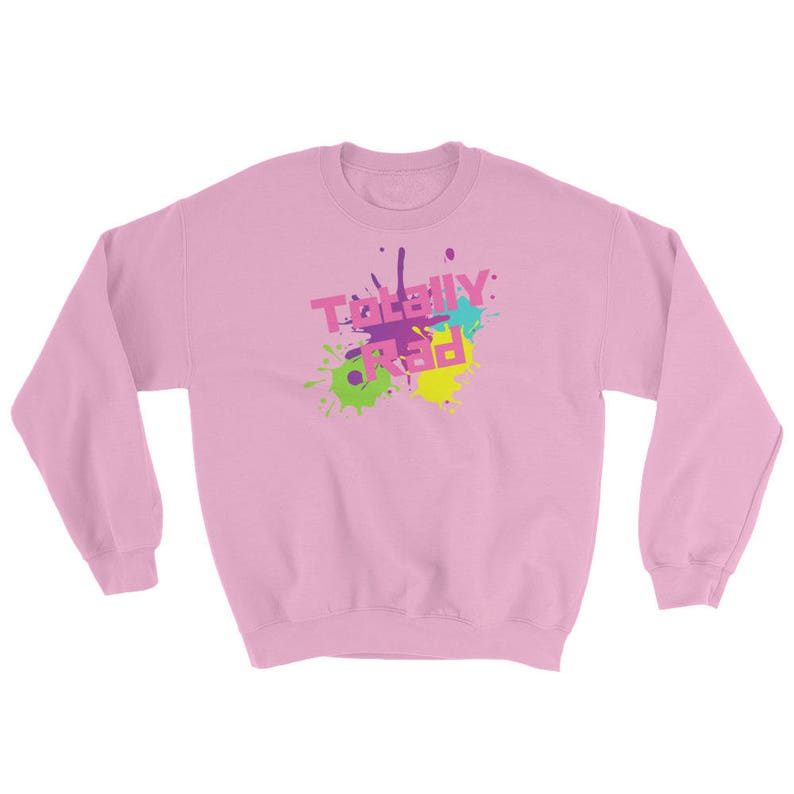 May include: A light pink sweatshirt with long sleeves. The front features the text "TOTALLY RAD" in a colorful, splattered design with pink, purple, green, blue, and yellow accents. The sweatshirt is a casual, comfortable style.