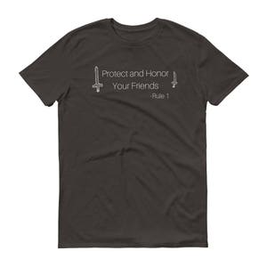 May include: Dark gray t-shirt with the text "Protect and Honor Your Friends - Rule 1" in white. The design includes stylized sword illustrations on either side of the text. A casual, everyday wear tee.