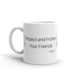 Pu&ograve; includere: Tazza in ceramica bianca con la scritta "Protect and Honor Your Friends - Rule 1" in nero. La tazza presenta una grafica a spada su entrambi i lati del testo. Un design semplice ma audace per una tazza da caff&egrave; o da t&egrave;.