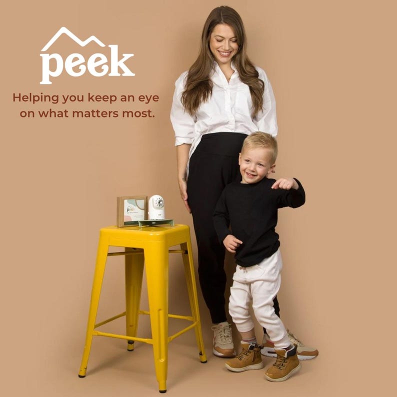 Op de afbeelding: Een gele metalen kruk met een babyfoon en een ingelijste foto. Een vrouw en een jong kind staan ernaast. De tekst "peek" en "Helping you keep an eye on what matters most" zijn in de afbeelding te zien.