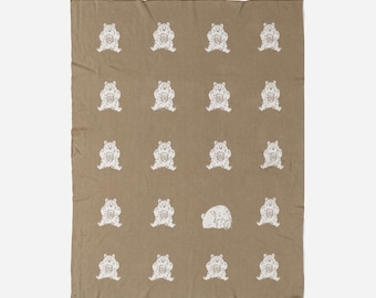 May include: A brown throw blanket with a repeating pattern of white bears holding mugs. One bear is lying down.