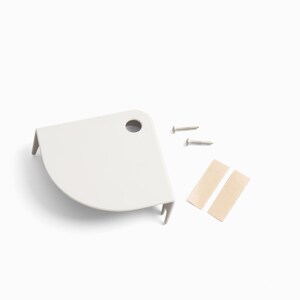 May include: A white, corner-shaped shelf bracket with a pre-drilled hole, two silver screws, and two beige adhesive strips. The bracket has a curved front edge and two small support tabs.