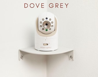 Op de afbeelding: Een witte en beige babyfoon met de tekst "INFANT OPTICS" is gemonteerd op een duifgrijze hoekplank. De monitor heeft een cameralens en diverse kleine lampjes. De woorden "DOVE GREY" staan boven de monitor.