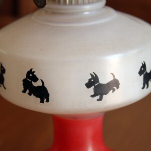 May include: White oil lamp with a red base and black silhouette images of Scottish Terriers around the top.