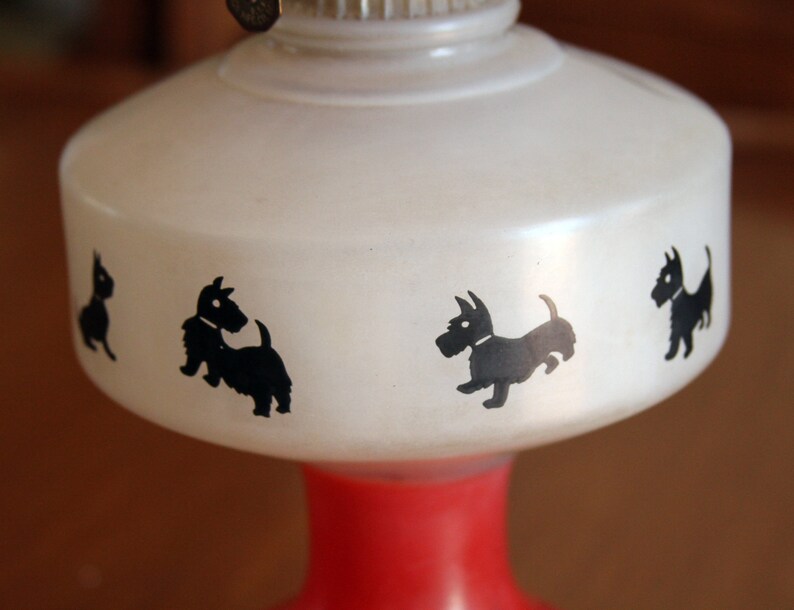 May include: White oil lamp with a red base and black silhouette images of Scottish Terriers around the top.